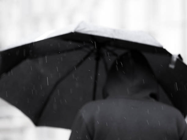 istock Man in black under a black umbrella in the rain. Focus on raindrops 1150952598