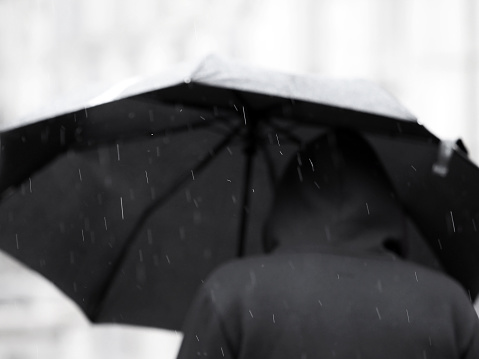 Man in black under a black umbrella in the rain. Focus on raindrops