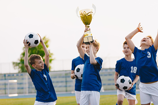 Boys are cheering for their team victory. Happy kids celebrating success in sports youth tournament. Boys holding golden cup. Football school tournament for children