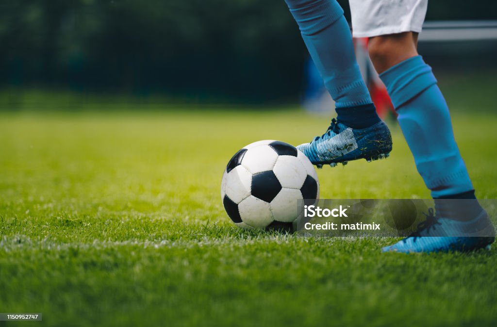 Close up of legs and feet of football player in blue socks and shoes running and dribbling with the ball. Soccer player running after the ball. Sports venue in the background Soccer Stock Photo