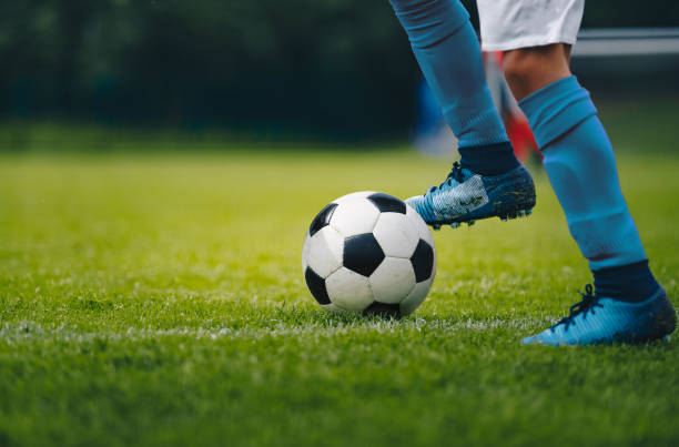 關閉穿著藍色襪子和鞋子的足球運動員的腿和腳, 用球運球。足球運動員追球。背景中的體育場館 - soccer 個照片及圖片檔