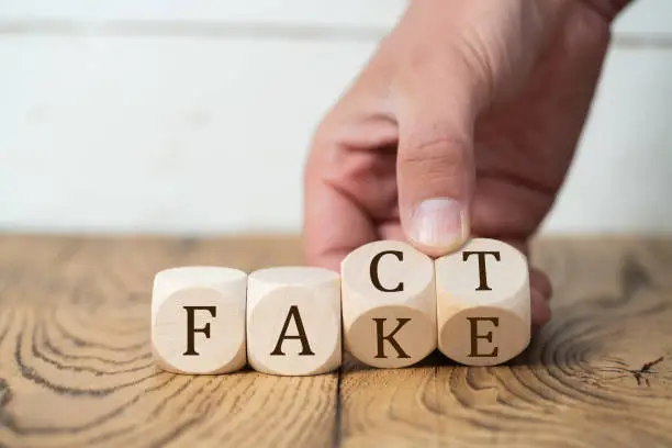 hand is turning two of four cubes, changing the word FACT to FAKE on wooden background