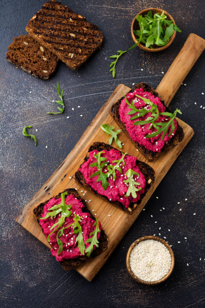 istock Bruschetta with beetroot hummus, arugula and sesame seeds on dark concrete background. Top view. 1150956095