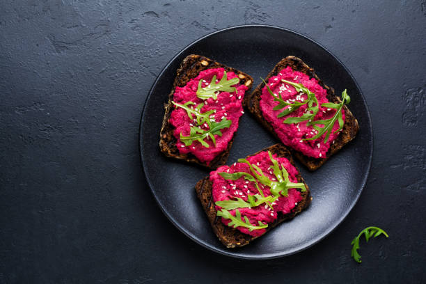 istock Bruschetta with beetroot hummus, arugula and sesame seeds on dark concrete background. Top view. 1150956555