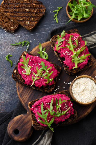 istock Bruschetta with beetroot hummus, arugula and sesame seeds on dark concrete background. Top view. 1150957146