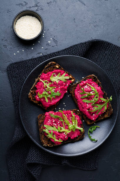 istock Bruschetta with beetroot hummus, arugula and sesame seeds on dark concrete background. Top view. 1150957290