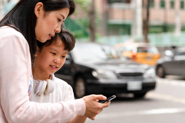 A mother and daughter waiting for a taxi that they booked through a ride sharing service on their mobile phone.