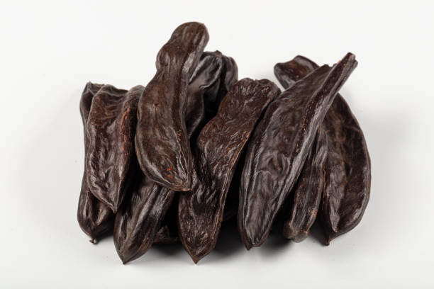 istock Carob molasses and carob pods (harnup) on white background. 1150963864