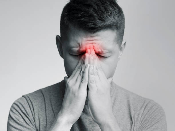 Sad man holding his nose because sinus pain Sinus pain, sinusitis. Sad man holding his nose, black and white photo with red sore zone sinusitis photos stock pictures, royalty-free photos & images