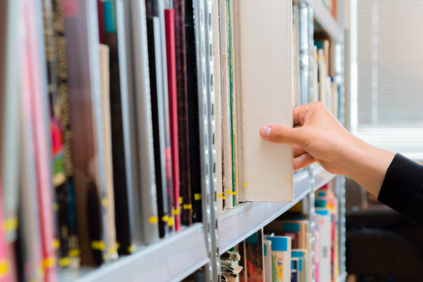 istock Young student picking a book from the shelf in the library. Preparing for exams, young man searching for or choosing a book in the public library in university 1150970584