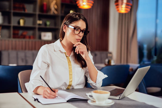istock Woman taking notes in agenda and looking at laptop while sitting in cafe. 1150973391