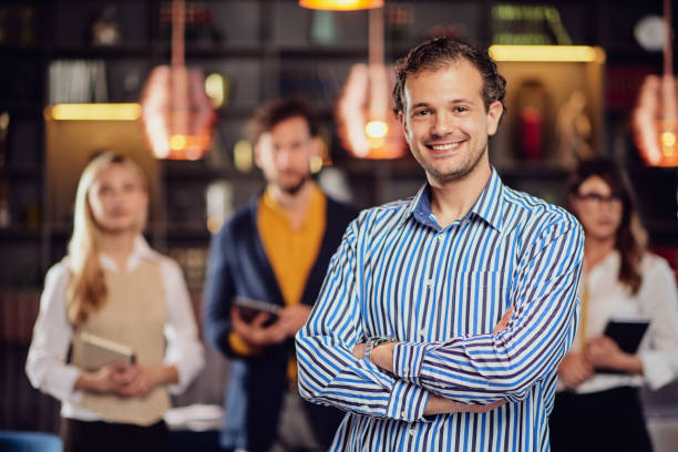 Young attractive arab businessman standing at restaurant with arms crossed. In background his successful team posing.