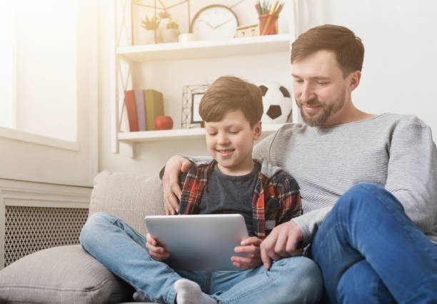 istock Father and son using tablet together on sofa at home 1150974671