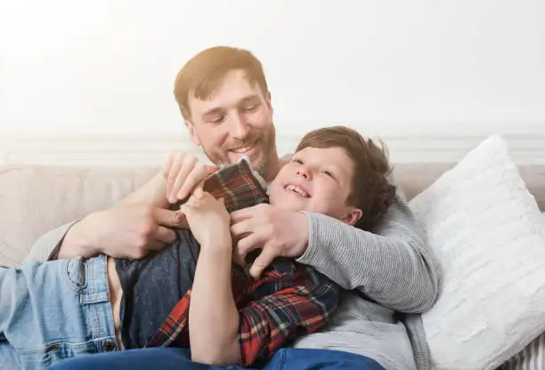Photo of Loving father having fun with his son on sofa