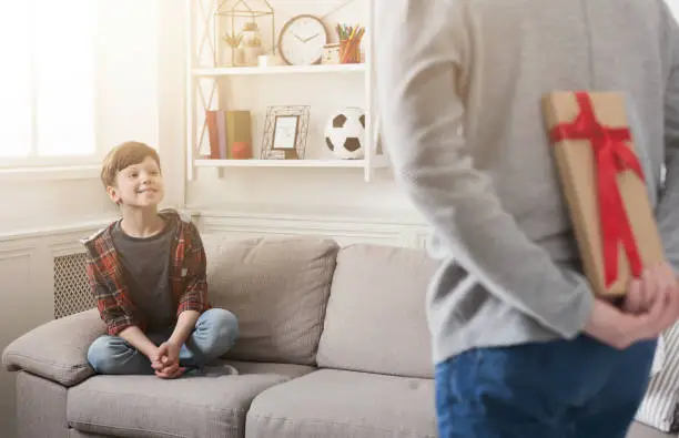 Father prepare birthday gift case to impressed son sitting on sofa at home