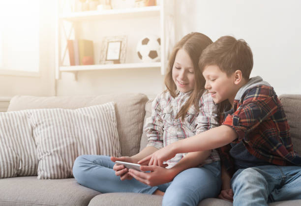 istock Two kids playing on smartphone on sofa at home 1150974687