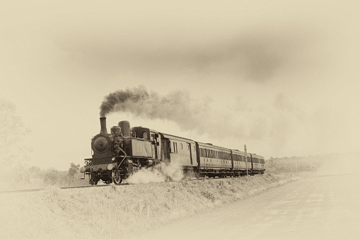 Ancient steam train running on tracks in the countryside. Old photo filter applied.