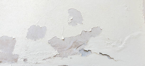 istock Old weathered painted wall background texture. White dirty peeled plaster wall with falling off flakes of paint. 1150977792