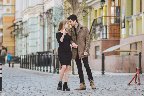 istock Urban modern young love couple walking romantic talking talking, holding hands on a date. Young multicultural Turkish brunette and Caucasian couple on old european street. Autumn spring weather 1150980430