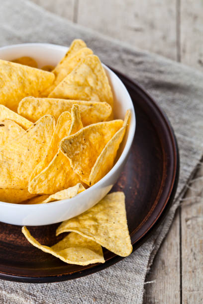 istock Mexican nachos chips in white bowl on brown ceramic plate on linen tablecloth. 1150989275
