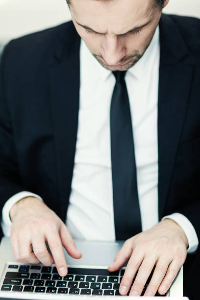 opinião de ângulo elevado do homem envelhecido médio concentrado no terno, na camisa branca e no laço que datilografam no computador portátil - shirt and tie typing communication part of - fotografias e filmes do acervo