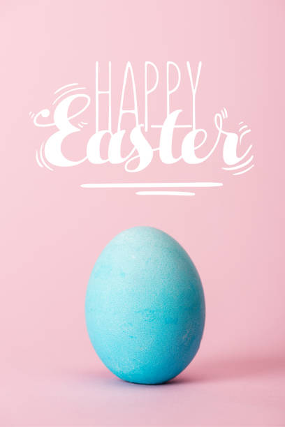 istock blue chicken egg on pink background with happy Easter lettering 1150998591