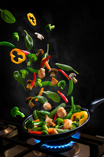 Vegetables and chicken fly through the air into a frying pan