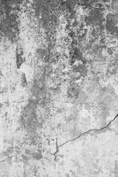 Dirty, old stone wall with rough and cracked structures. At the bottom right, a strong crack in the wall. Concrete wall background in portrait format, in industrial design.