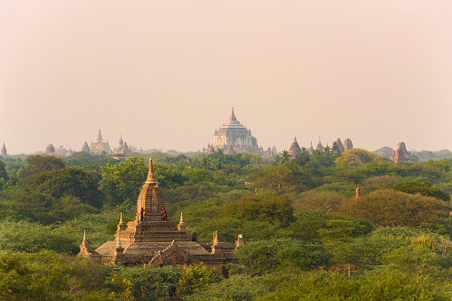 Bagan, Myanmar, March 25, 2019. A unidentified Burmese couple, wearing a traditional Longyi, are taking photos and selfies from the roof of one of many temples in Bagan. Stunning view of the Bagan Archeological Zone during sunset. The Bagan Archaeological Zone is a main attraction in Myanmar and over 2,200 temples and pagodas still survive to the present day.