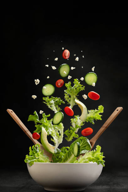 Salad ingredients with servers flying through the air, landing in a bowl - fotografia de stock
