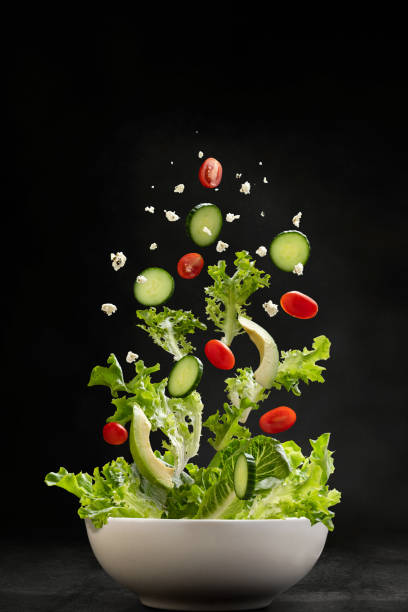 Salad ingredients flying through the air, landing in a bowl Salad ingredients with servers flying through the air, landing in a bowl cucumber photos stock pictures, royalty-free photos & images