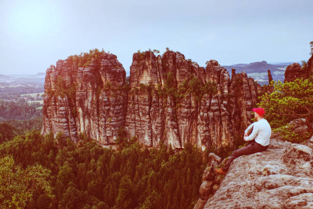 istock Man hiker with red cap on rock and looks at sharp mountain 1151026095