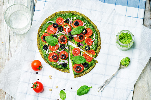 vegan broccoli zucchini pizza crust with spinach pesto, tomatoes, onion and olives. toning. selective focus