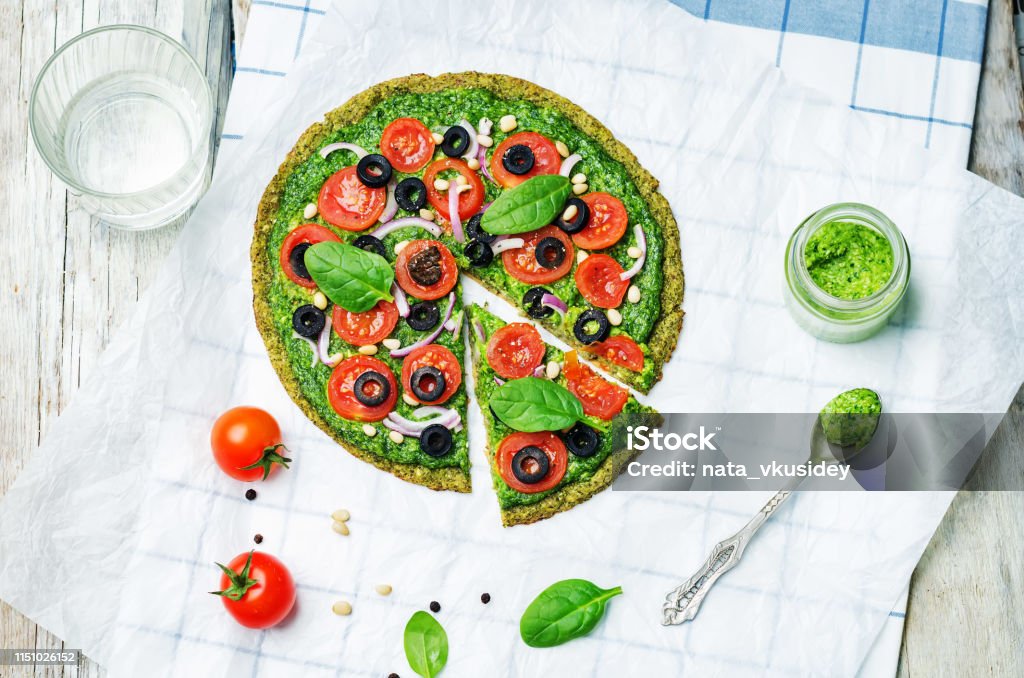 vegan broccoli zucchini pizza crust with spinach pesto, tomatoes, onion and olives vegan broccoli zucchini pizza crust with spinach pesto, tomatoes, onion and olives. toning. selective focus Pizza Stock Photo