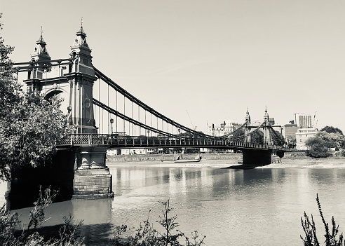 A black and white photo of Hammersmith Bridge taken from the south bank of the River Thames.