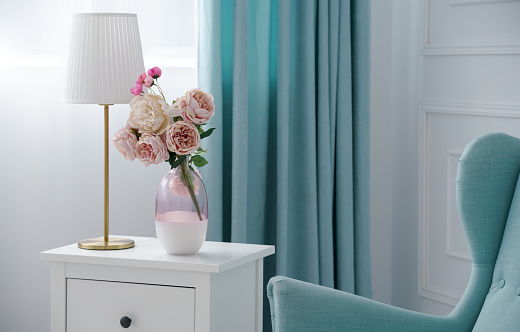 Pink Flower vase and golden table lamp with blue armchair and curtains