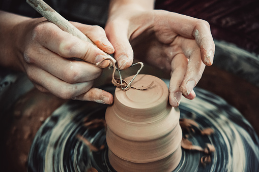 Master removes the top layer of clay on pot with a special tool.
