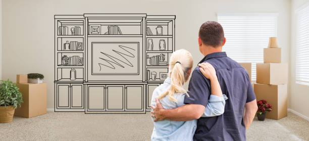 istock Couple Inside Empty Room with Moving Boxes Facing Entertainment Unit Drawing on Wall 1151042004