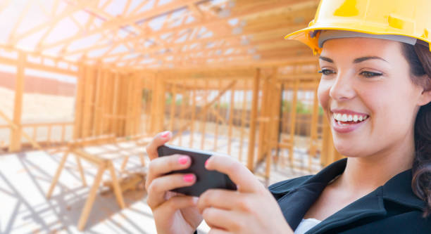 istock Smiling Female Contractor In Hard Hat Using Smart Phone At Construction Site 1151042008