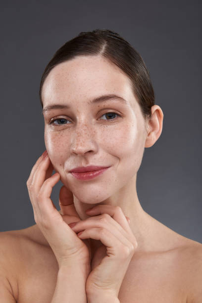 istock Smiling young woman with freckles touching her face 1151045700