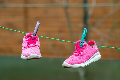 Pair of bright sport fitness sneakers hanged on clothespin at backyard after laundry outdoors. Preparartion for running training or marathon.