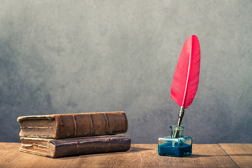 Pluma de Quill rojo vintage con tintero y libros viejos sobre fondo de pared de hormigón de mesa de madera. Estilo retro Instagram foto filtrada photo