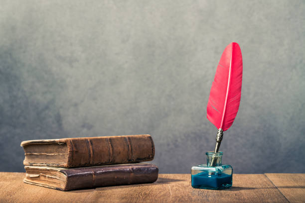 Vintage red quill pen with inkwell and old books on wooden table front concrete wall background. Retro instagram style filtered photo stock photo