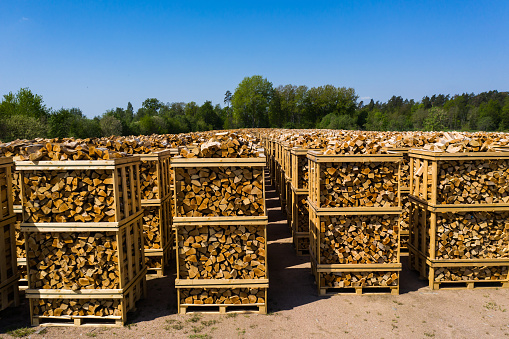 Rows of firewood stacked on pallets ready for transport. Part of surrounding landscape visible.