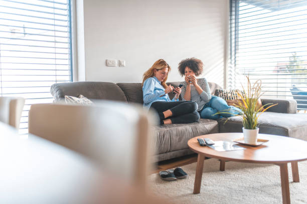 istock Woman sharing phone with friend sitting on sofa 1151053676