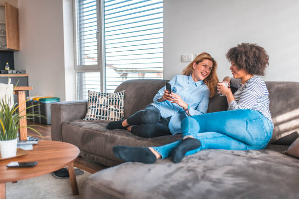 istock Woman sharing phone with friend sitting on sofa 1151053679