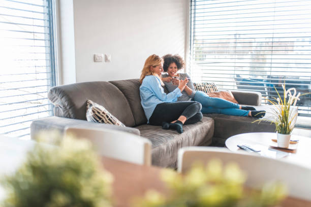 istock Woman sharing phone with friend sitting on sofa 1151053681