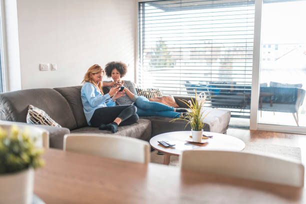 istock Woman sharing phone with friend sitting on sofa 1151053683