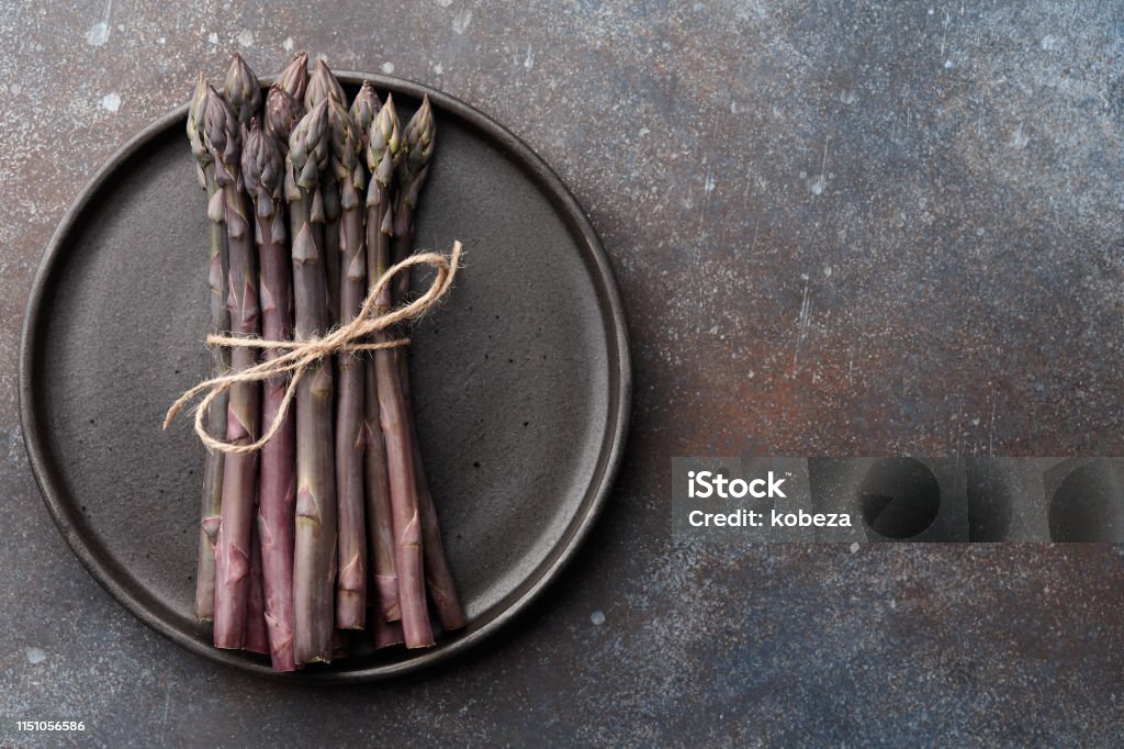 Bunch of purple asparagus on rusty background Bunch of fresh purple asparagus in plate on rusty textured background, copy space Asparagus Stock Photo