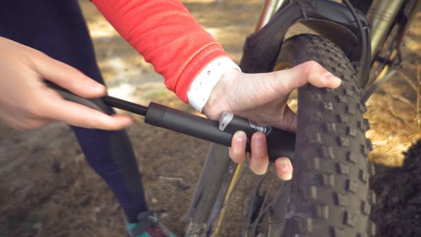 Young caucasian woman athlete tourist cyclist uses a hand tool, a bicycle pump to inflate air into a tire wheel mountain bike. Breakdown and quick repair of a bicycle in the countryside outside. joven mujer caucásica atleta ciclista turística utiliza una herramienta de mano, una bomba de bicicleta para inflar el aire en una bicicleta de montaña rueda de neumáticos. desglose y reparación rápida de una bicicleta en el campo al aire libre
